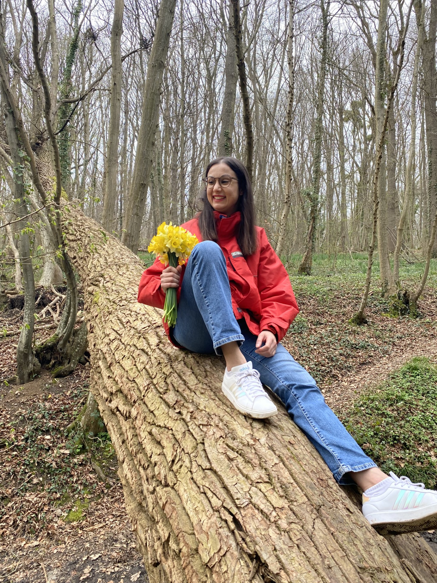 Honorine Lemaire assise sur un tronc dans un bois, tenant un bouquet de jonquilles